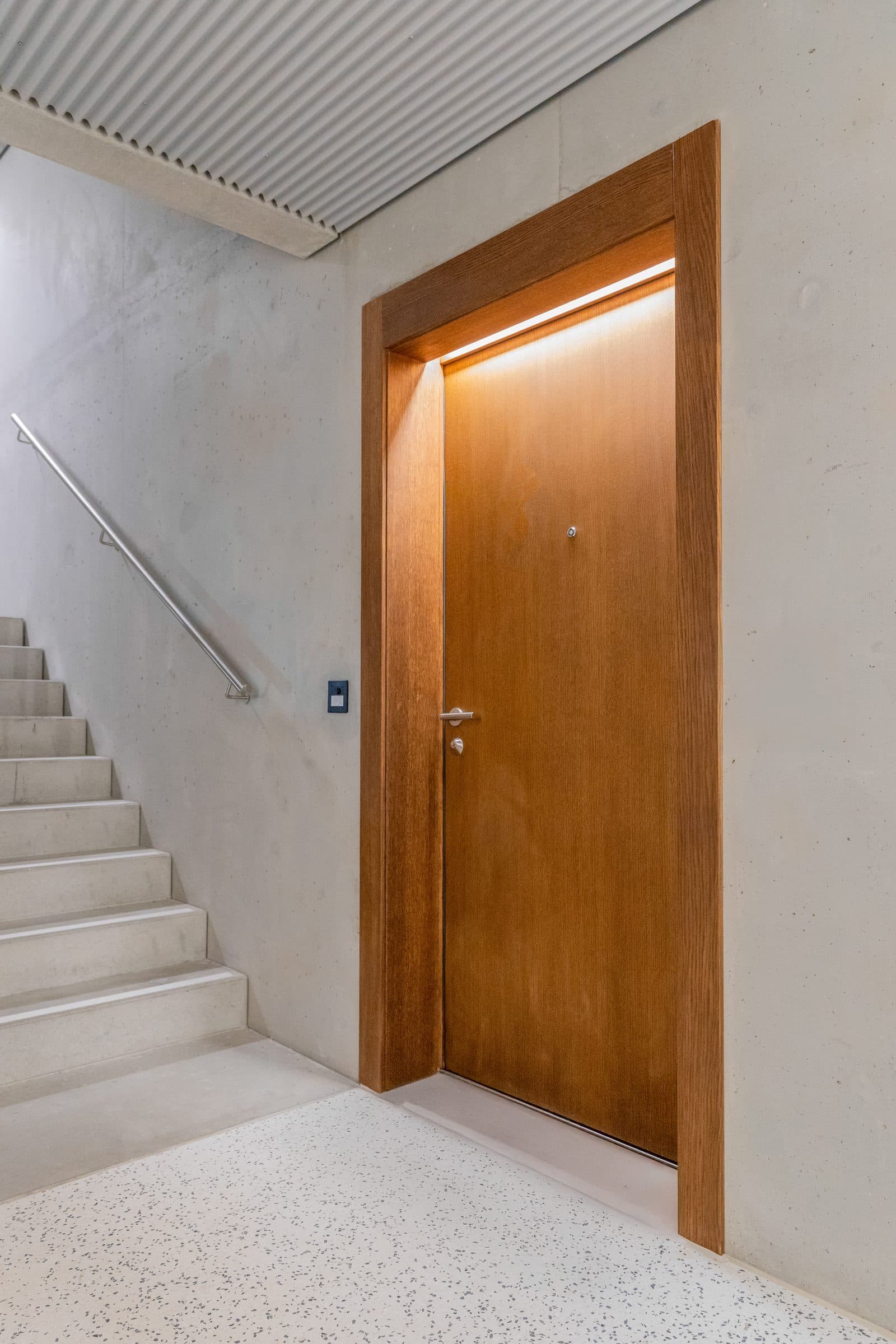 Oak entrance door set in a concrete stairwell, with an integrated light in the frame